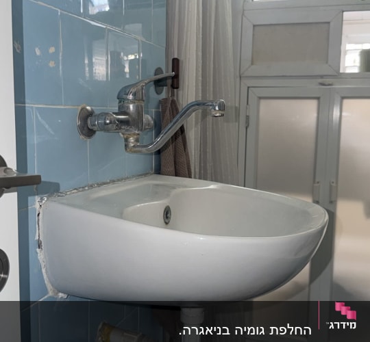 כיור רחצה תלוי מותקן בחדר רחצה עם ברז קיר וצנרת ניקוז